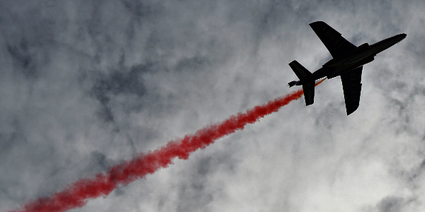 airplane flying high in the sky with red smoke trails behind it, signifying travel risks and dangers in thailand