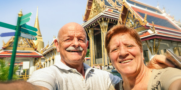 a happy expat couple taking a selfie outside a thai temple as they enjoy their retirement in thailand