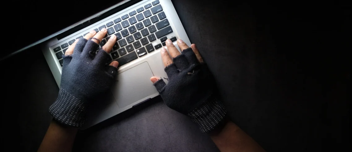 Hands wearing cut-off gloves typing on laptop computer with light from the screen shining