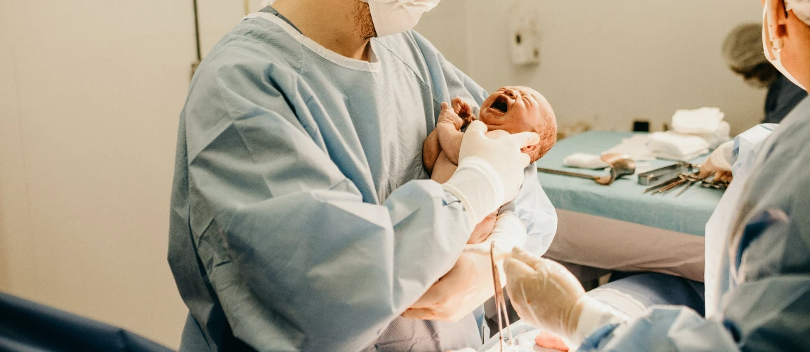 A doctor holding a newborn baby in an operating room