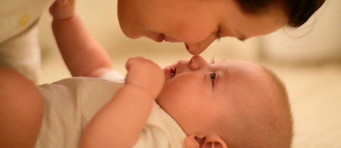 A mother and child eskimo kissing on a bed