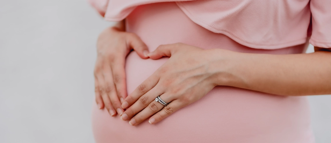A pragnant woman with a ring on her left hand placing hands on her belly