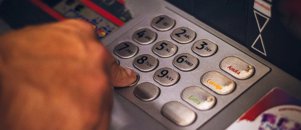 A hand typing numbers on an ATM