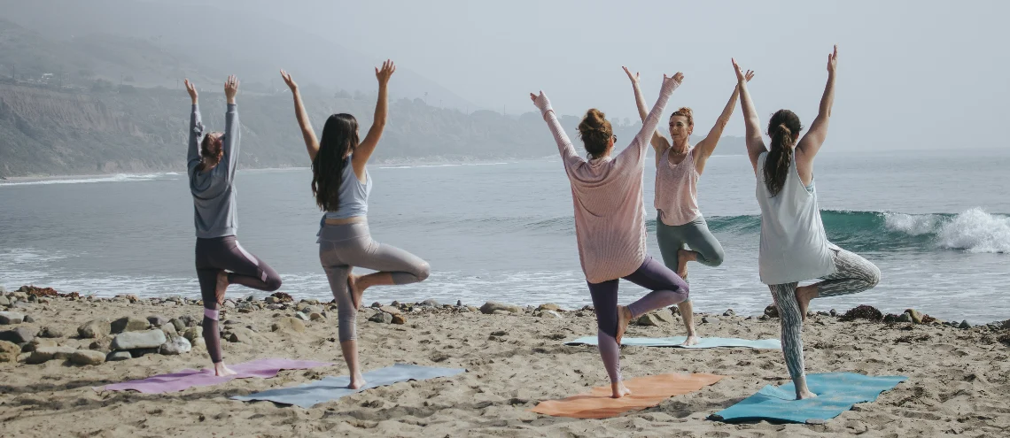 five woman doing yoga on a seashore