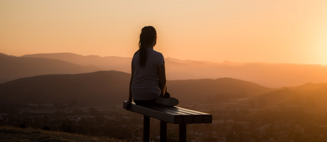 woman sitting on bench and viewing a mountain in the distant