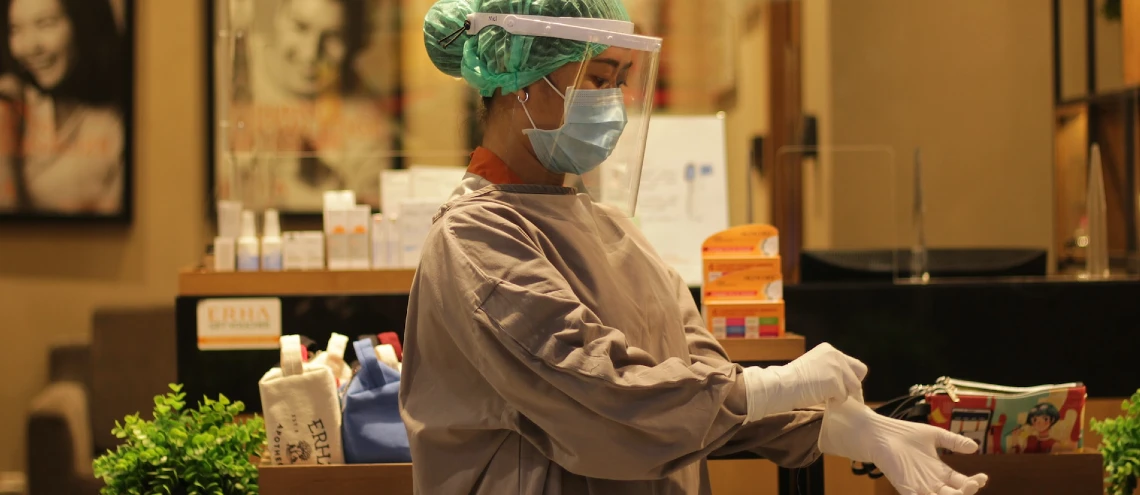 Nurse wearing protective medical gear putting on white gloves standing in clinic