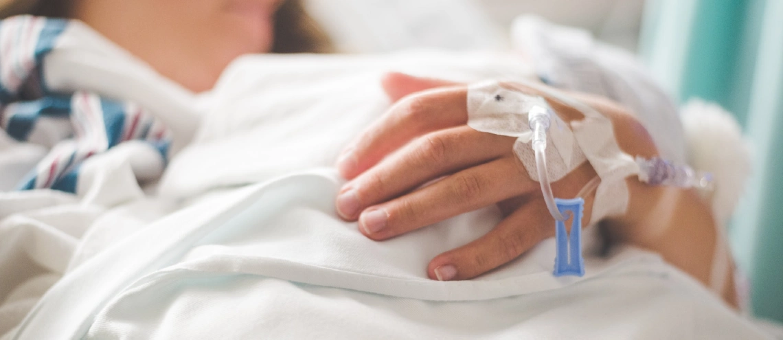 Person out of focus lying on hospital bed with IV drip coming out of hand