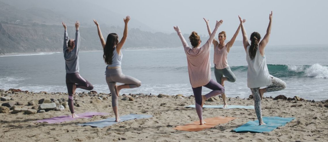 Women doing yoga by the beach during their mental health wellness retreat.