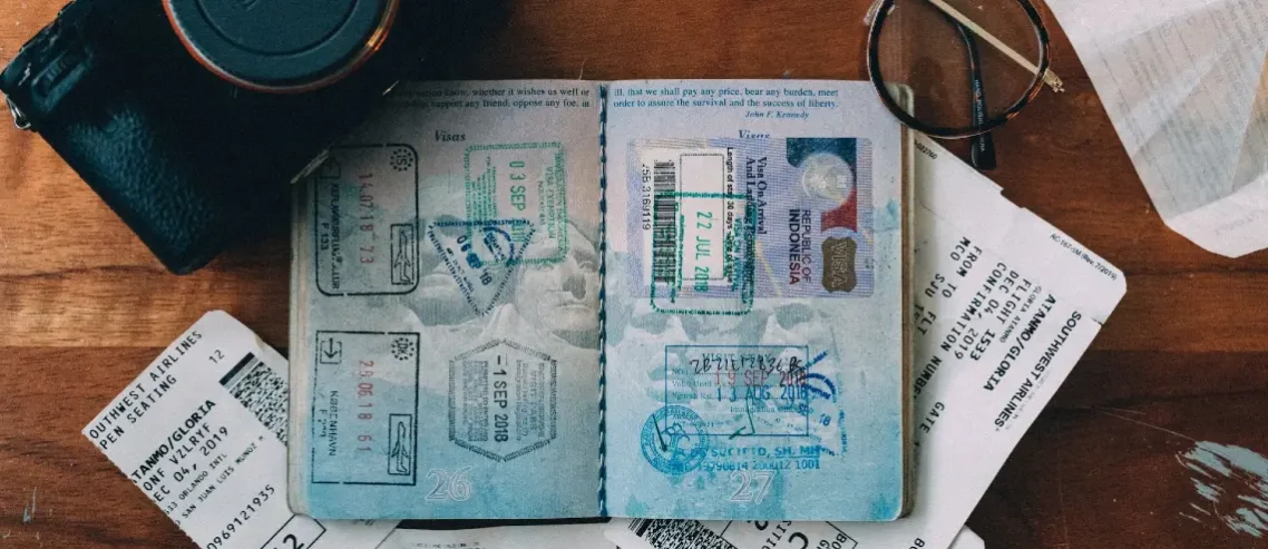 Open passport with visa stamps on a table with a camera and boarding pass