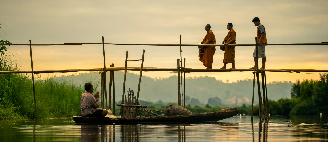 Two monks walking on a bridge with a Buddhist praying on a boat 