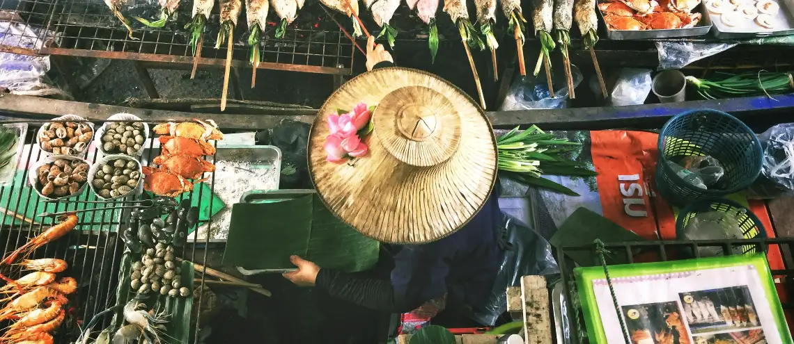 A merchant wearing a straw hat grilling fish on a boat