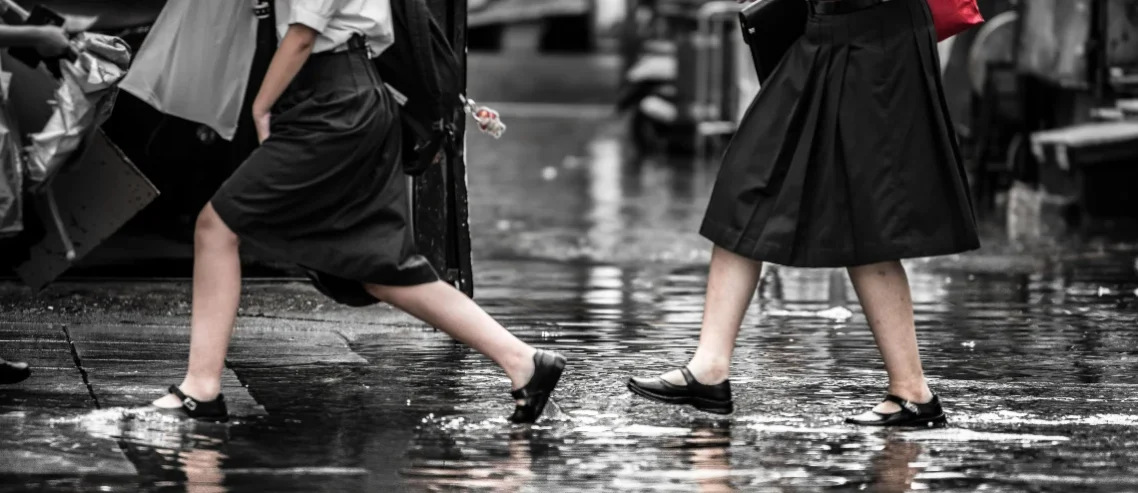 Two female students crossing the street without socks because of heavy rain